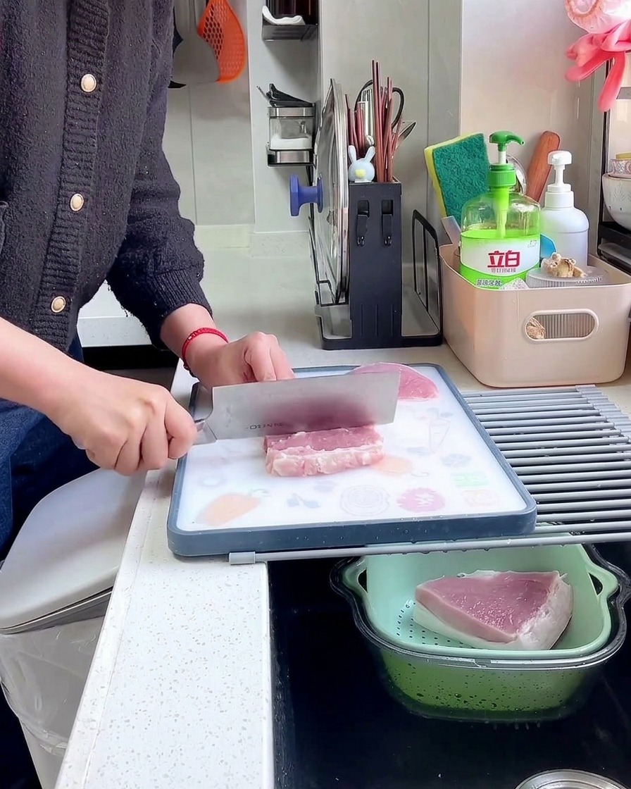 Una mano sostiene un hacha de cocina y usa el lomo de la hoja para golpear y ablandar un filete de cerdo crudo.
