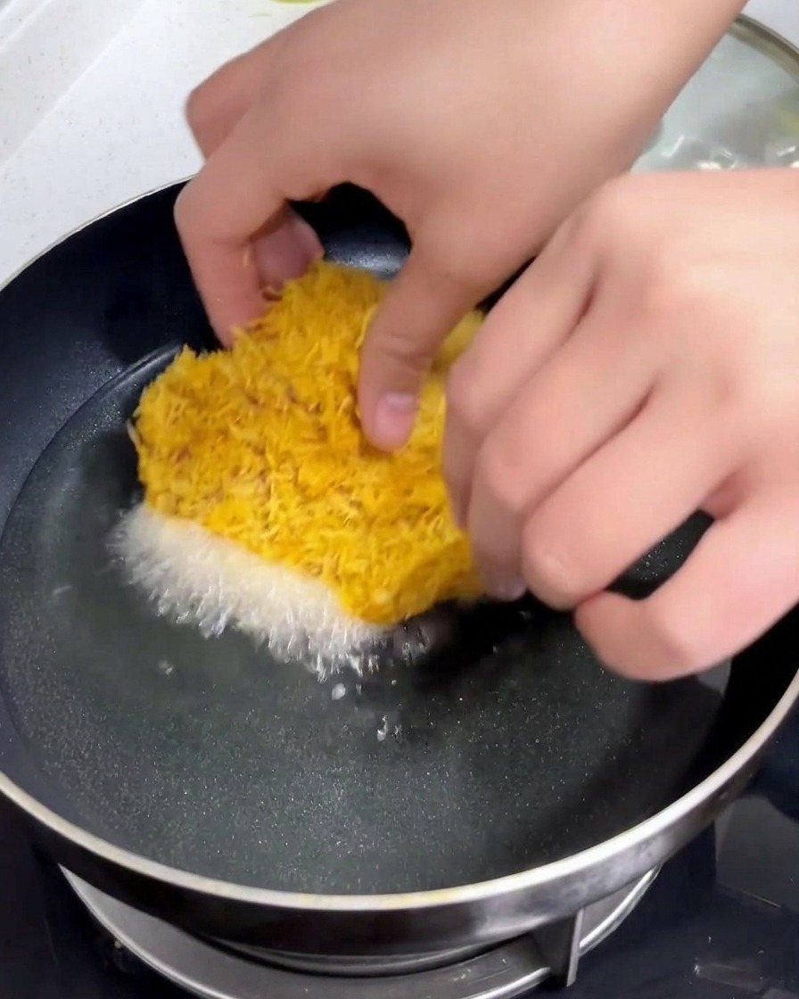 Una chuleta de cerdo empanada se sumerge con cuidado en una sartén con aceite caliente reluciente.