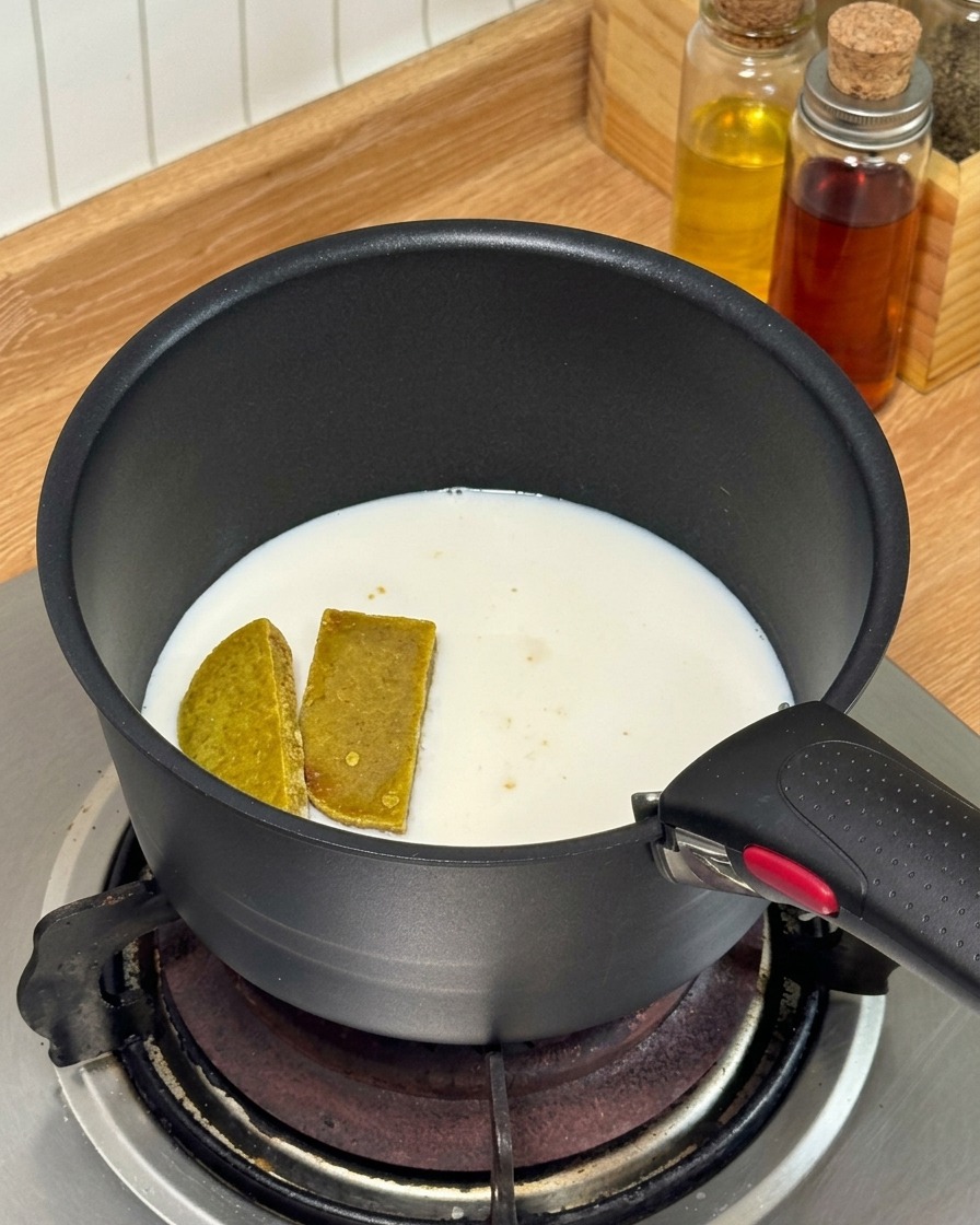 Cubos de curry y leche calentándose en una pequeña cacerola negra sobre una estufa de gas.
