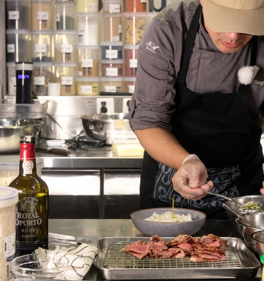 Un chef vertiendo una pequeña cucharada de aceite de cebolleta transparente sobre un bol de arroz blanco, con carne laminada reposando cerca en una rejilla.