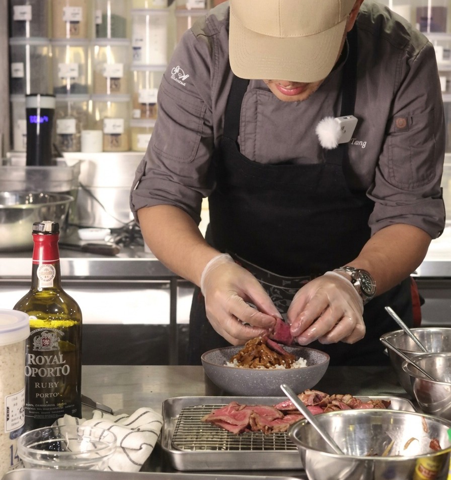 El chef colocando una lámina de ternera a término medio en la base de un bol de arroz lleno de cebollas caramelizadas.