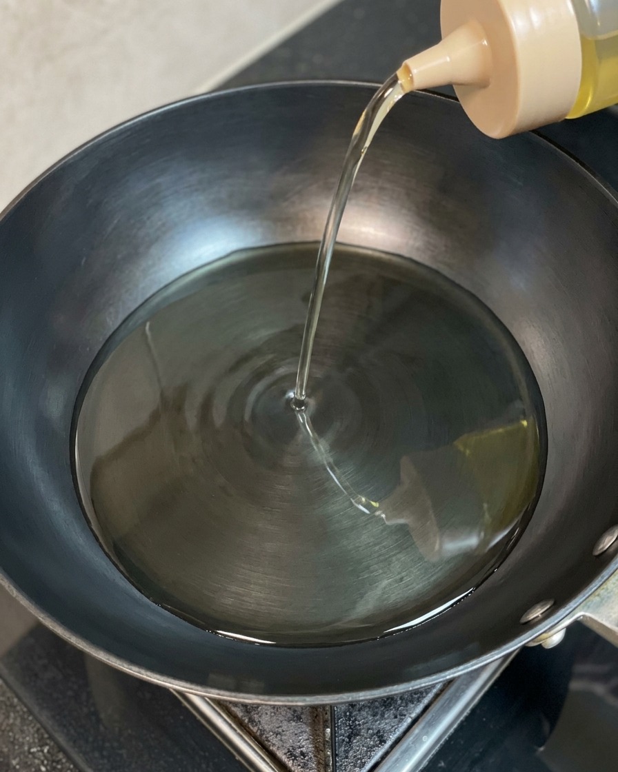 Aceite de cocina transparente vertiéndose desde una botella exprimible en un wok oscuro y caliente.