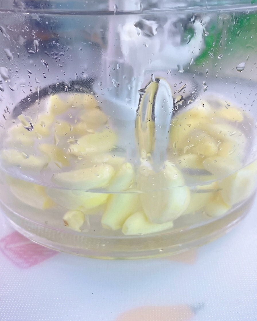 Dientes de ajo pelados y sal sumergidos en agua dentro del vaso de una licuadora transparente.