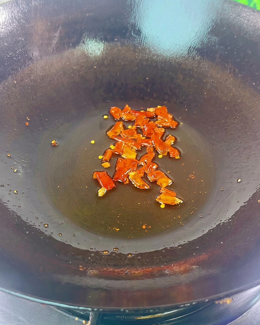 Trozos de chile rojo seco y frijoles negros chisporroteando en el fondo de un wok oscuro con una ligera capa de aceite.