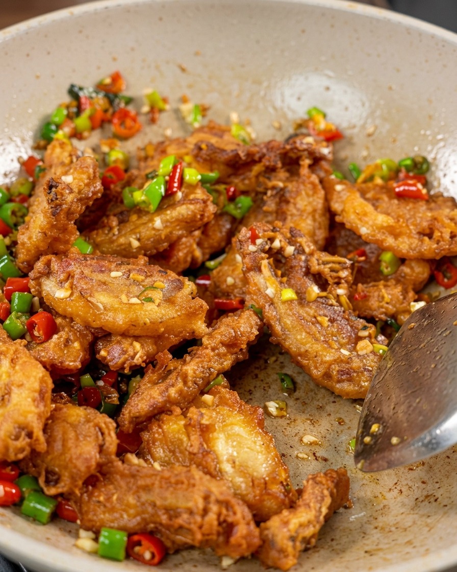 Un primer plano de panceta de cerdo crujiente, pimientos rojos y verdes y ajo siendo salteados en un wok con semillas de sésamo visibles.