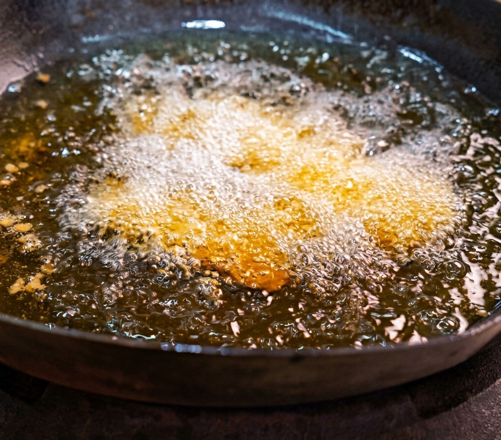 Láminas de panceta marinada friéndose en un wok con aceite caliente y burbujeante.