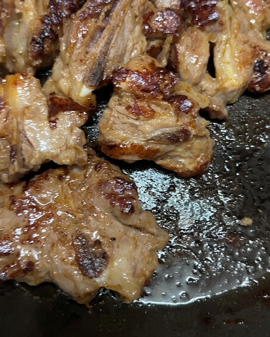 Costillas de cerdo cocinándose en una sartén, volteadas para mostrar una superficie bien dorada y caramelizada.