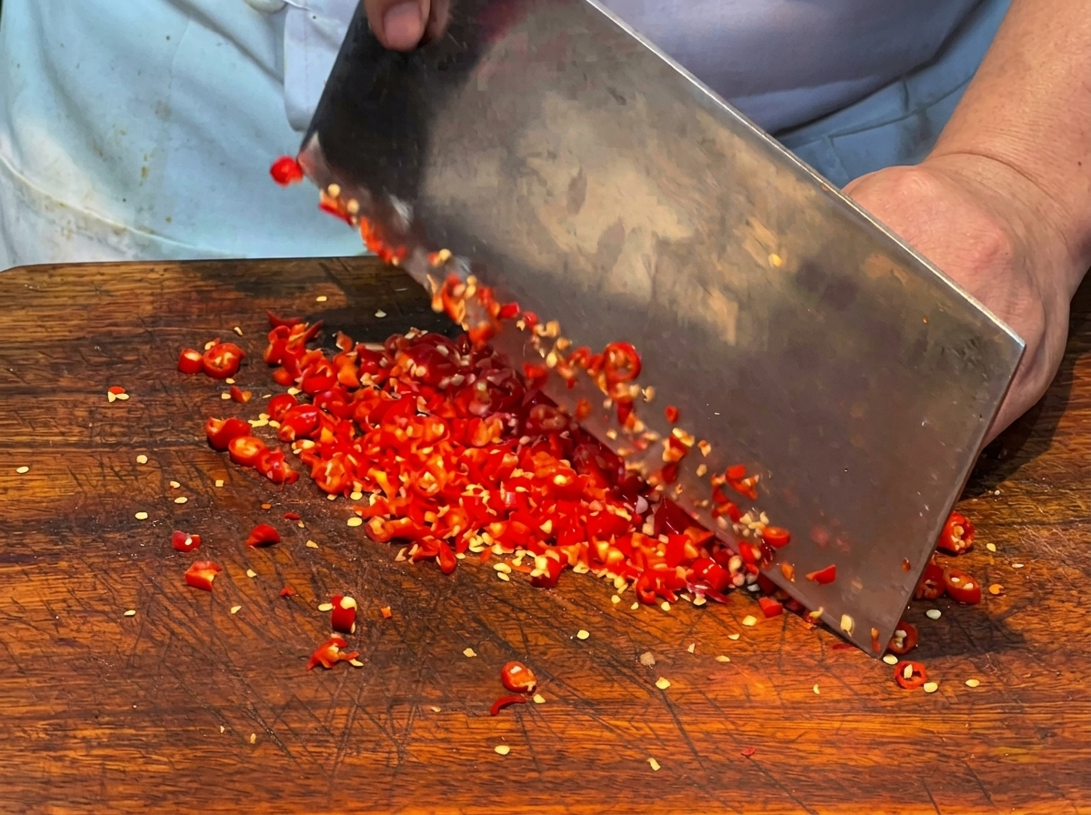 Primer plano de chiles rojos frescos siendo finamente picados con un hacha de cocina en una tabla de cortar.