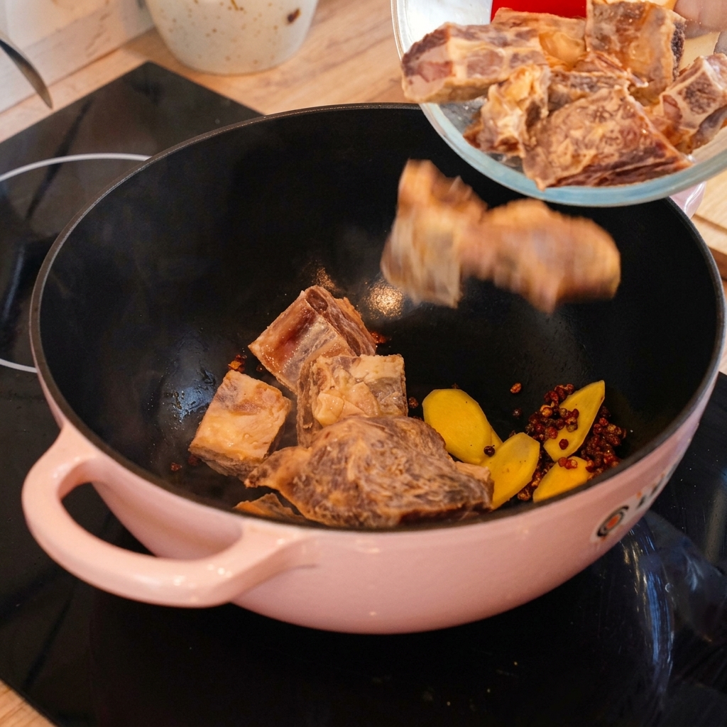 Trozos de costillas de cerdo curadas vertiéndose desde un bol de cristal a una olla rosa para sofreírlos con jengibre y pimienta.