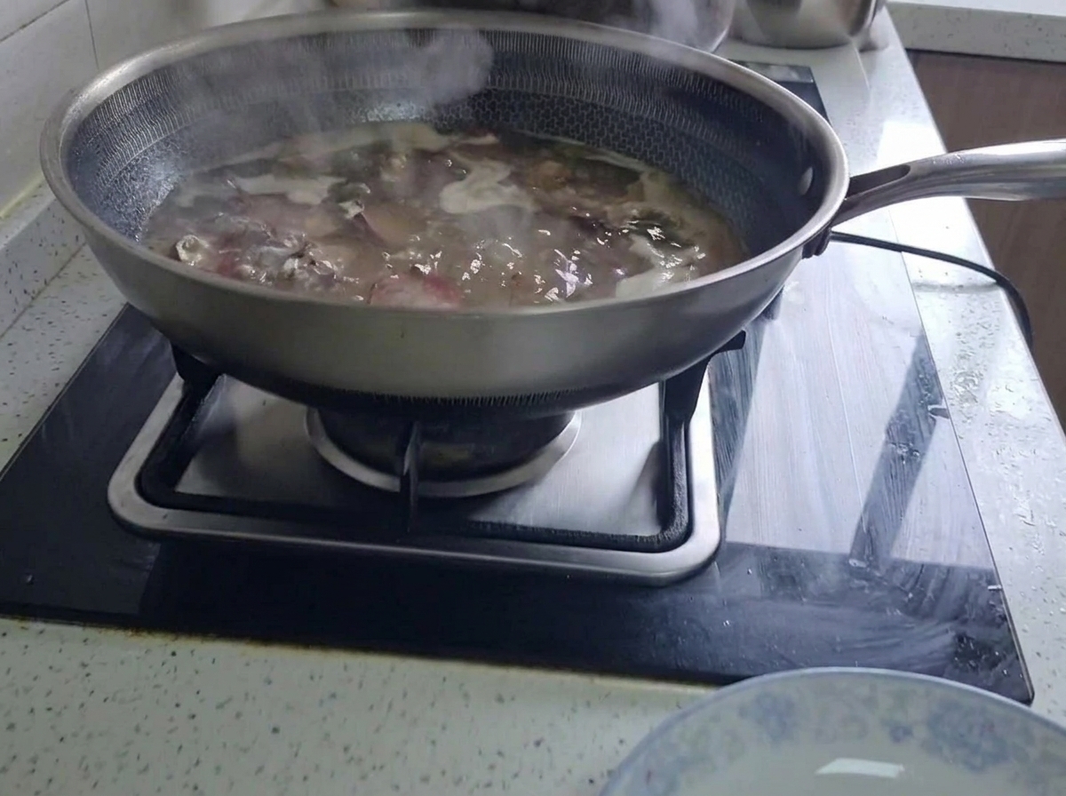 Costillas de cerdo curadas hirviendo a fuego lento en un wok grande lleno de agua sobre una estufa de cocina.