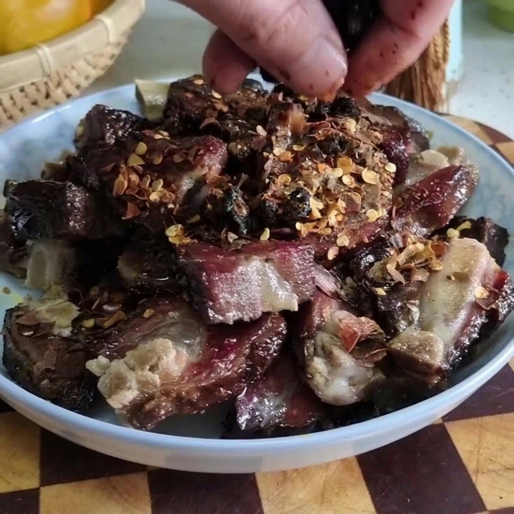 Primer plano de una mano esparciendo frijoles negros fermentados sobre un plato de costillas de cerdo curadas troceadas y cubiertas con copos de chile.