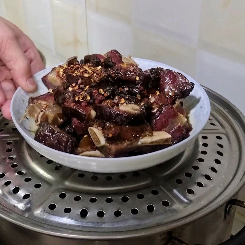 Una mano colocando un plato de costillas de cerdo curadas sazonadas sobre una rejilla metálica de vapor dentro de una olla.