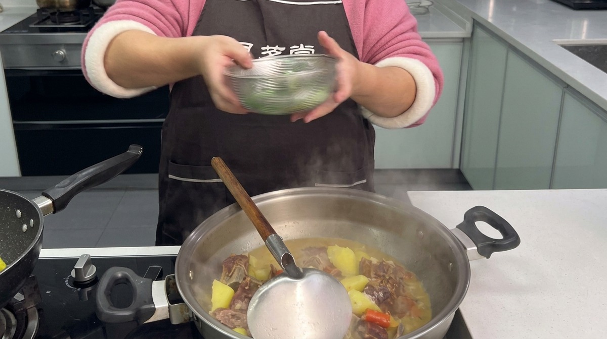 Brotes de ajo verde troceados siendo añadidos desde un cuenco transparente a un wok humeante lleno de estofado de costillas de cerdo curadas y patatas.