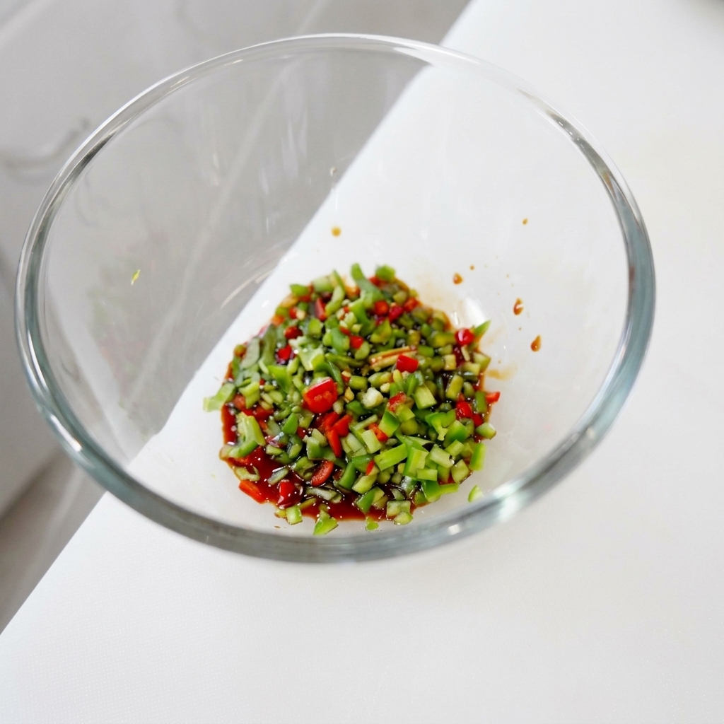 Una mezcla vibrante de chiles verdes y rojos finamente picados junto con cilantro remojados en una base líquida oscura y brillante dentro de un tazón de vidrio.