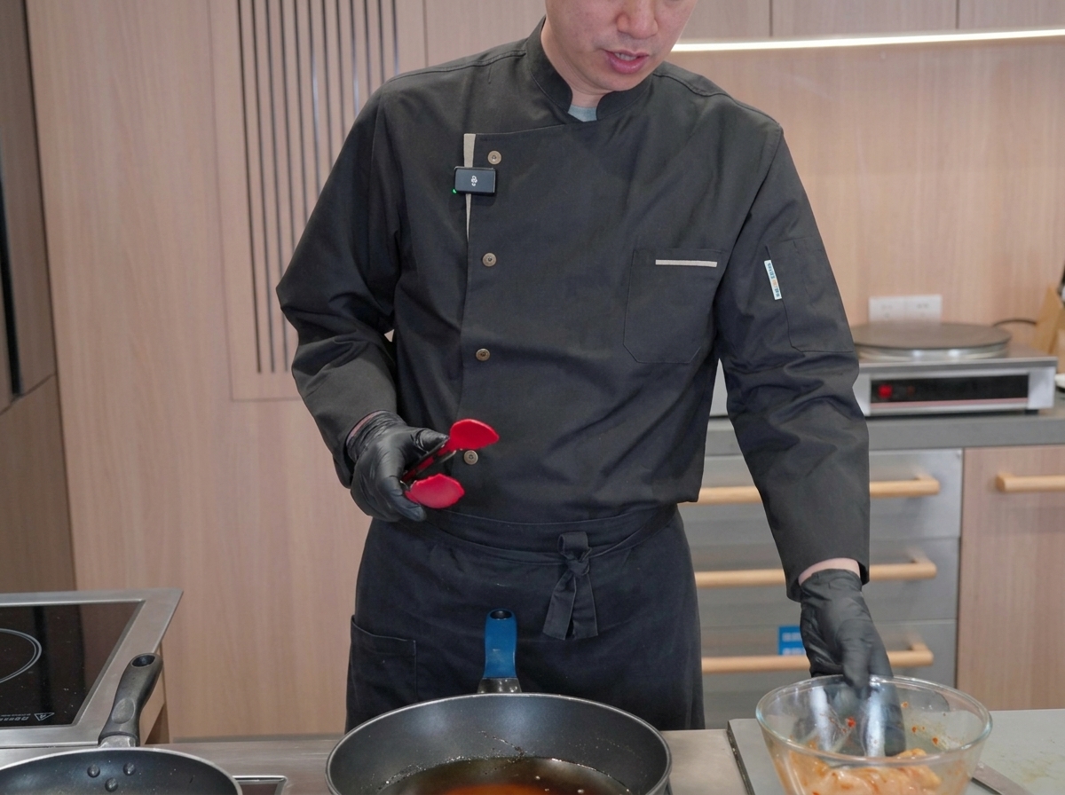 Trozos de calamar marinado cocinándose dentro de una sartén grande llena de aceite caliente y burbujeante mientras el chef controla el proceso de fritura.