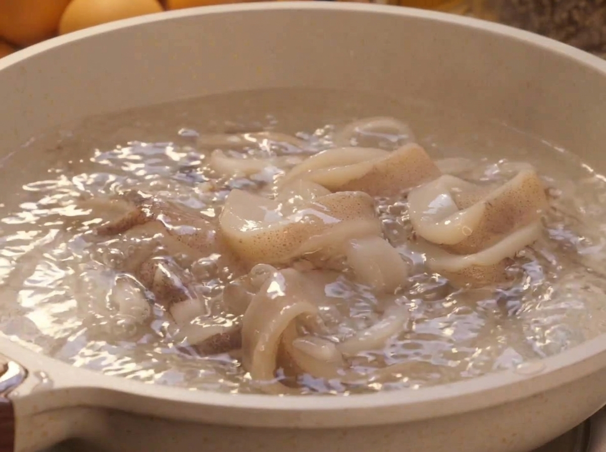 Anillos de calamar blanco fresco escaldándose dentro de una olla con agua hirviendo.