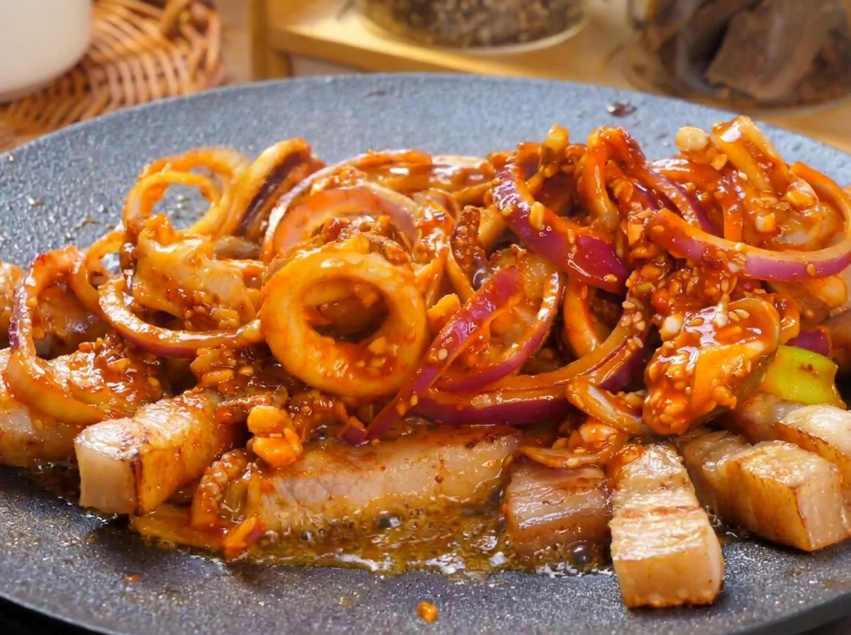Una plancha caliente llena de un salteado picante de panceta y calamar burbujeando con fuerza, cubierto con rodajas de chile verde.