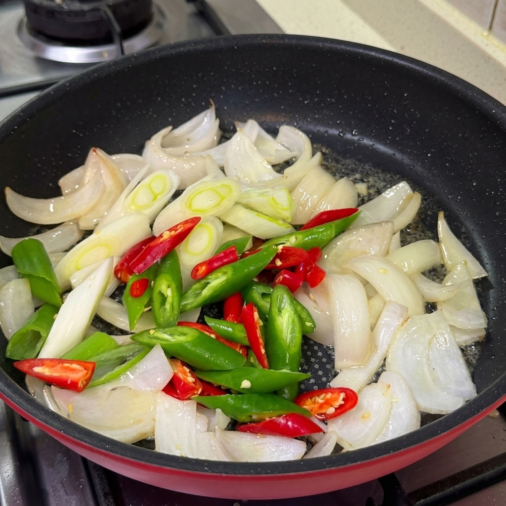 Chiles verdes y rojos en rodajas, cebolletas y ajo picado cocinándose en una sartén junto con las cebollas.
