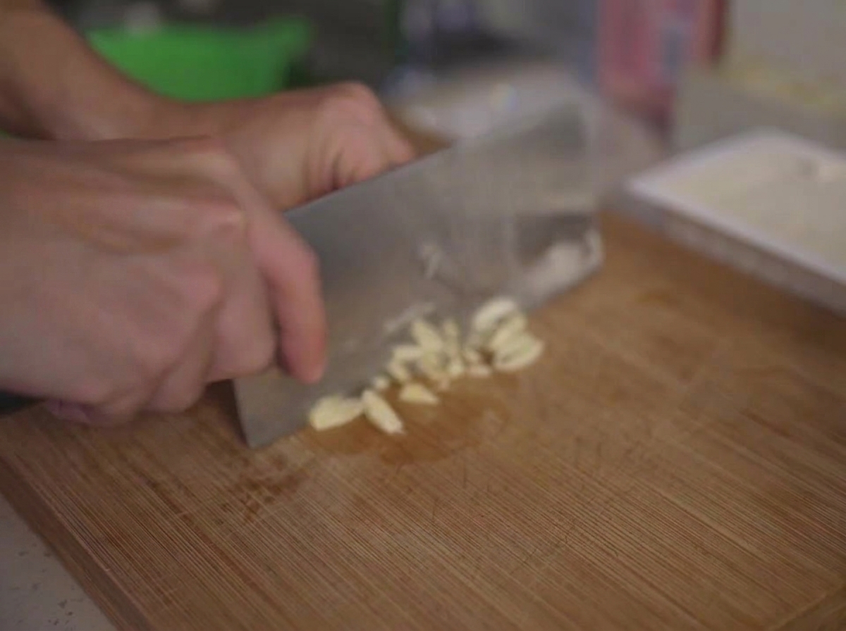 Ajo picado finamente en una tabla de cortar de madera con un cuchillo de cocina.