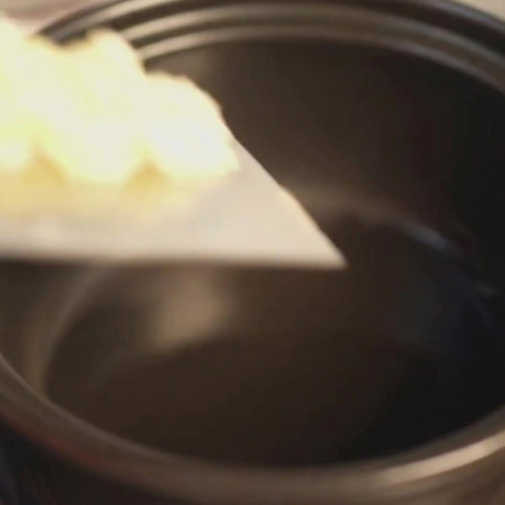 Ajo finamente picado siendo añadido a una olla de barro negra precalentada con aceite brillante.