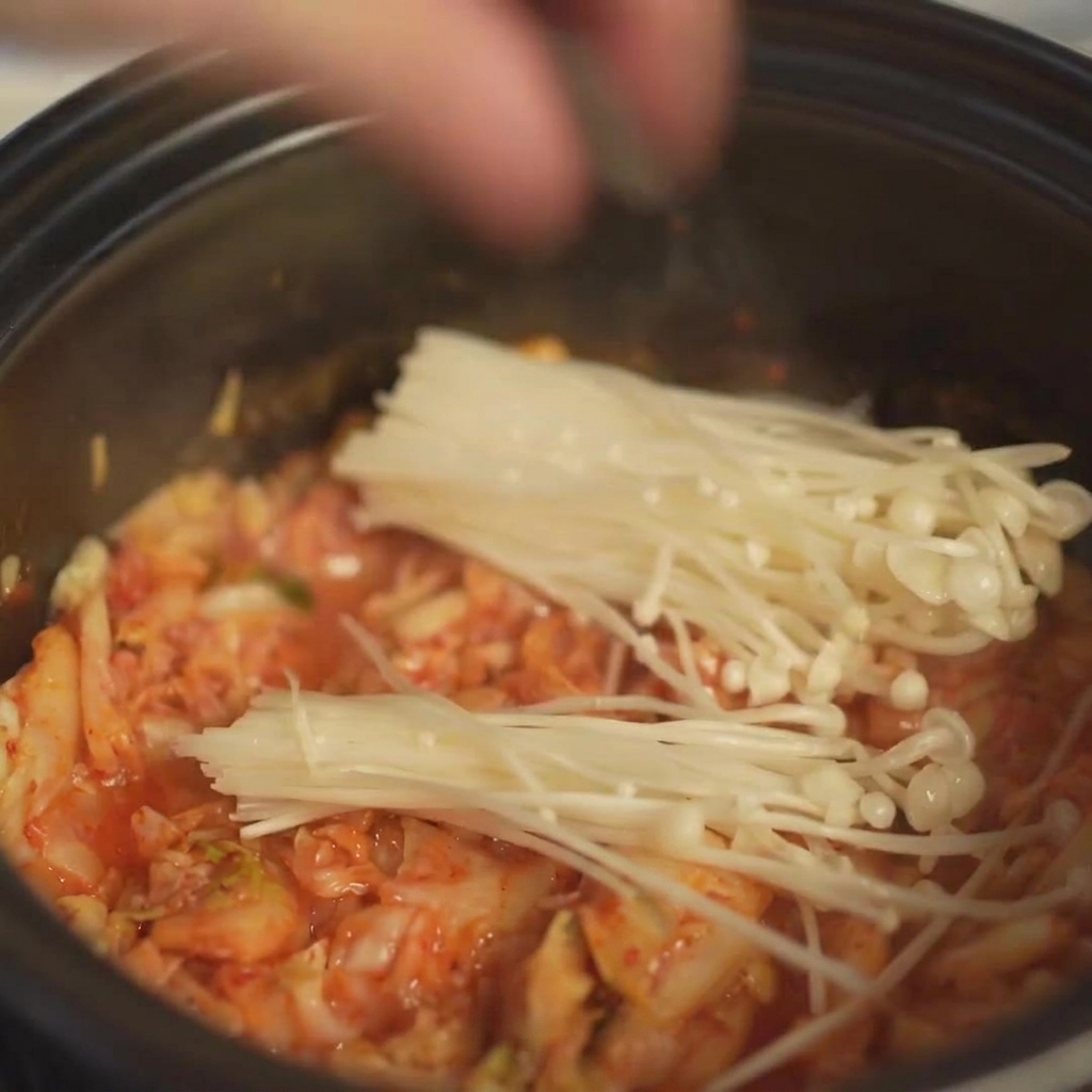 Colocando un manojo de hongos enoki frescos en la olla sobre el kimchi.