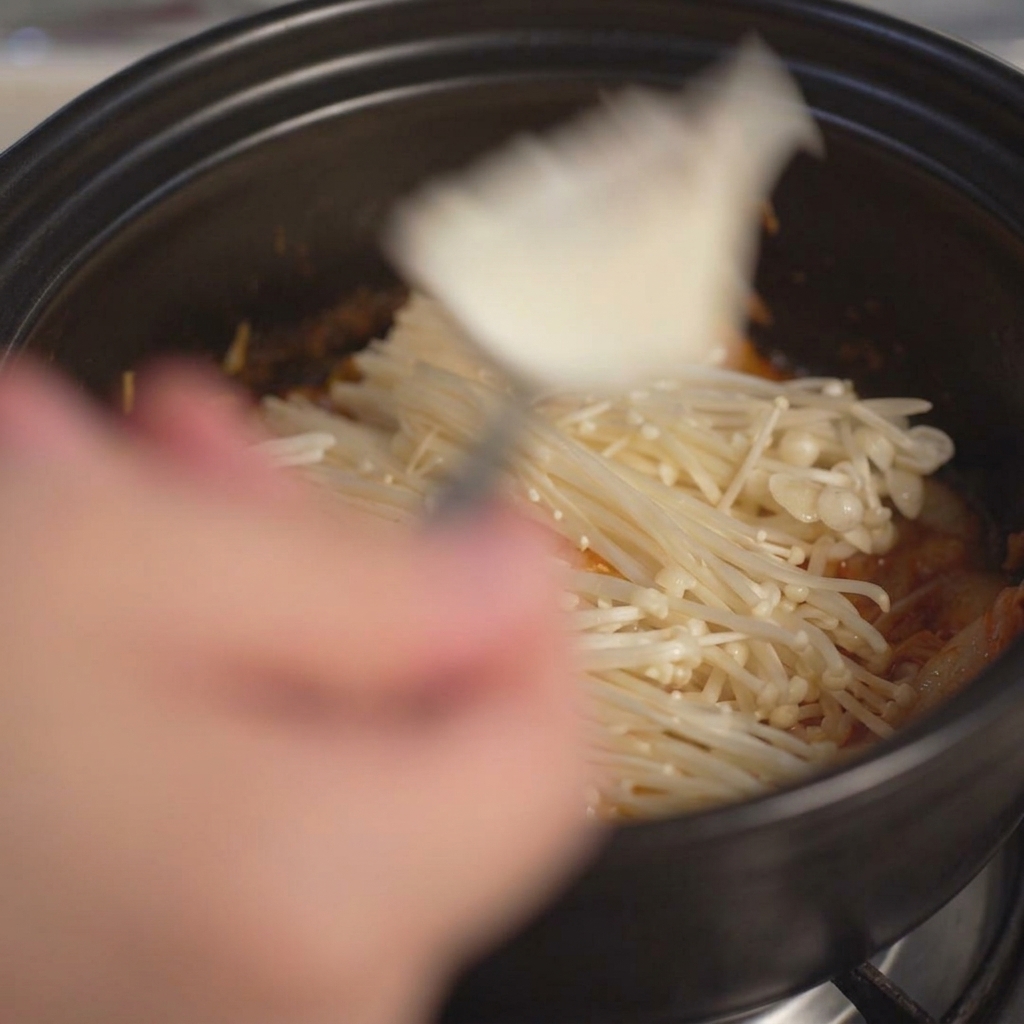 Añadiendo grandes trozos de tofu blanco suave en la olla con una cuchara.
