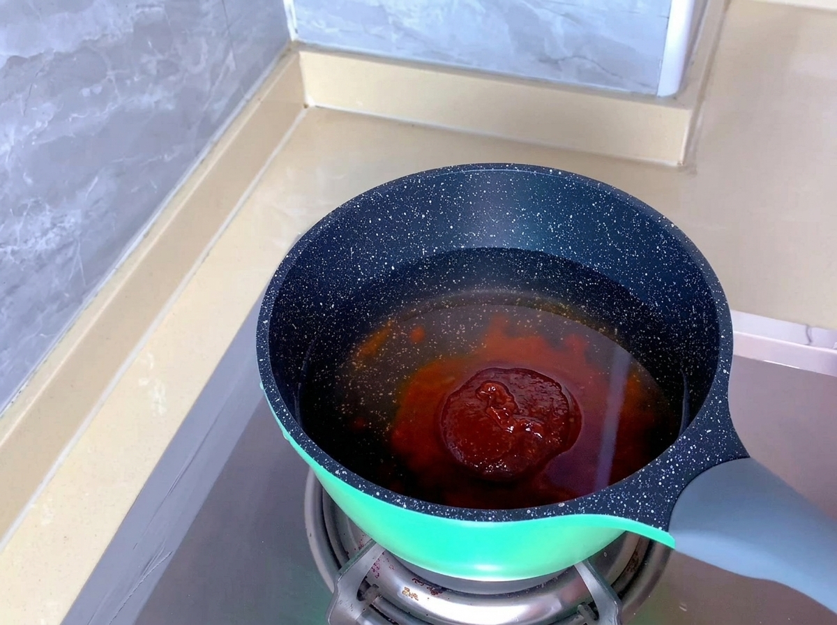 Una porción de pasta de sazonador de kimchi de color naranja rojizo sumergida en agua limpia dentro de una olla moteada.