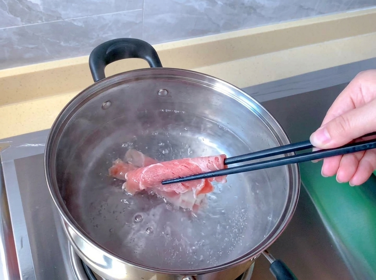 Unos palillos sumergen un rollo de ternera cruda y rosada en una olla de acero inoxidable con agua hirviendo.