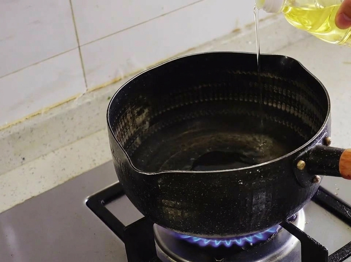 Aceite transparente vertiéndose desde una botella en una olla negra sobre el fuego de una estufa de gas.