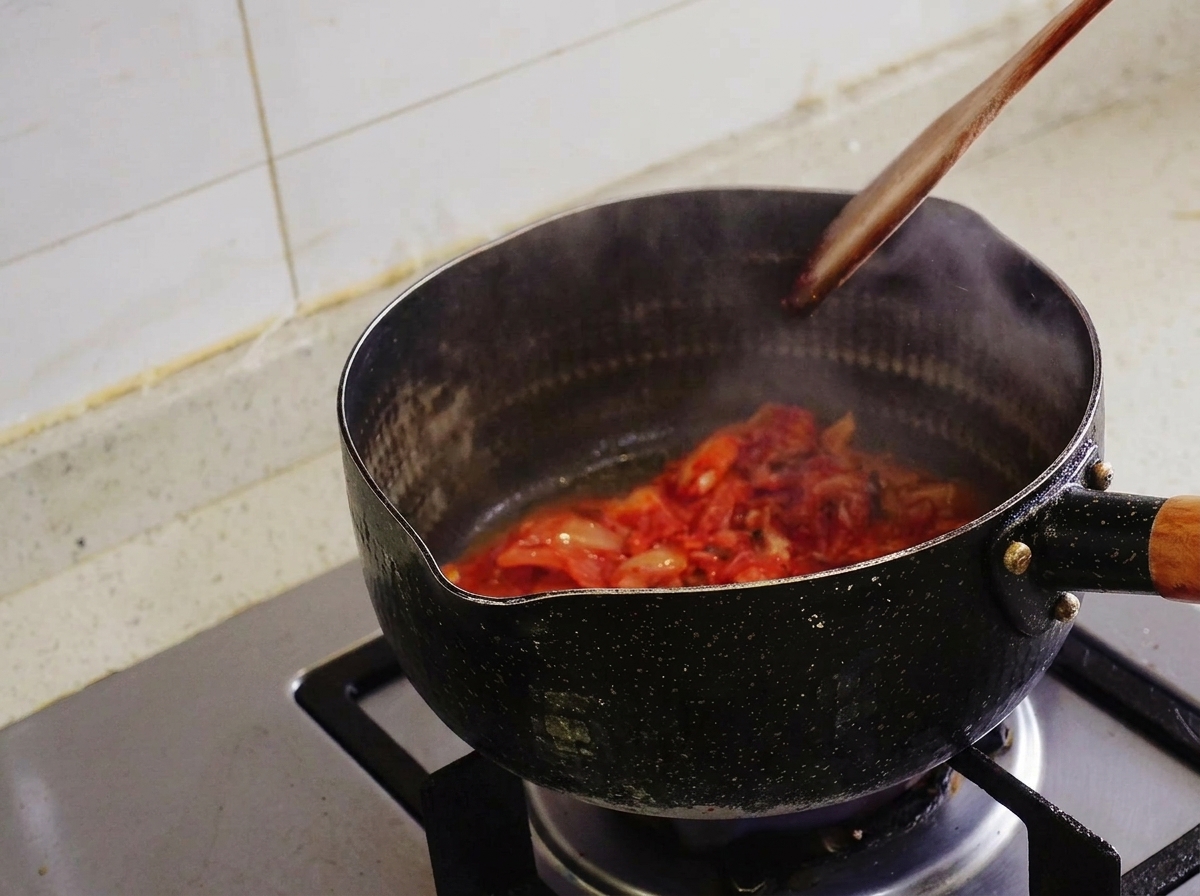 Kimchi siendo salteado con una espátula de madera dentro de una olla negra de la que sale vapor.