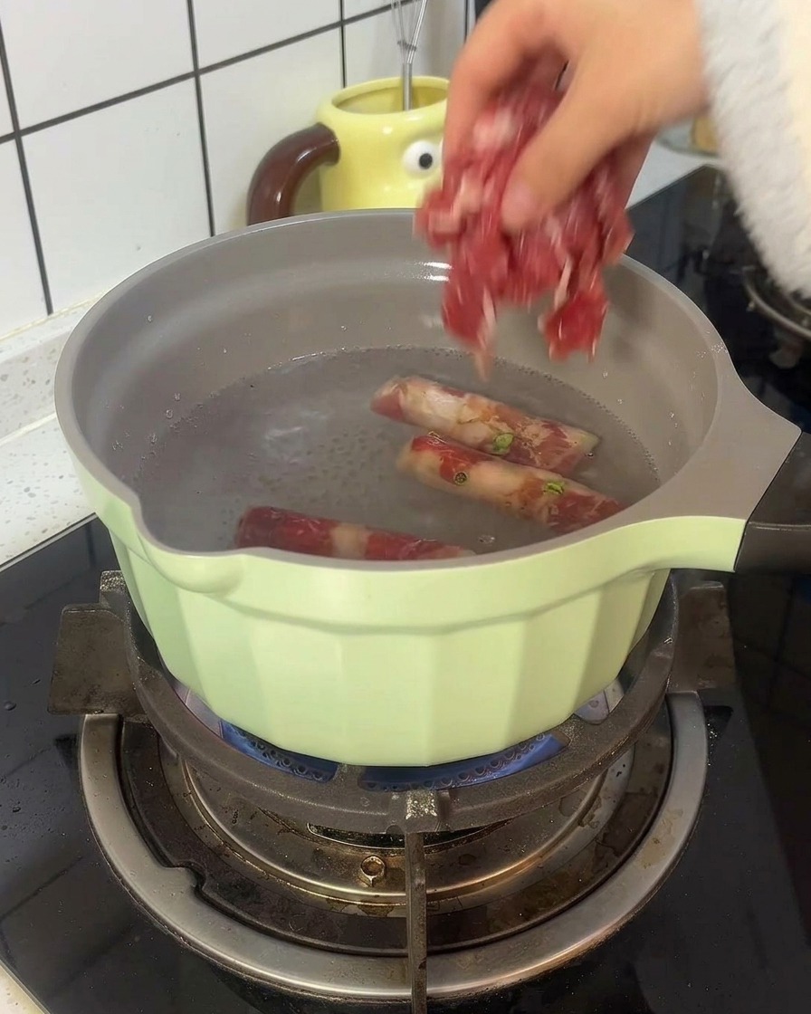 Rollos de carne de res blanqueándose en una olla verde claro con agua hirviendo.