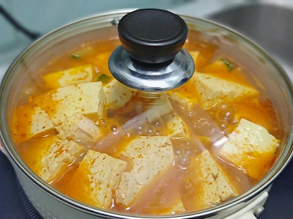 Una tapa de vidrio transparente cubriendo la olla de burbujeante sopa coreana de kimchi con tofu y carne mientras hierve.