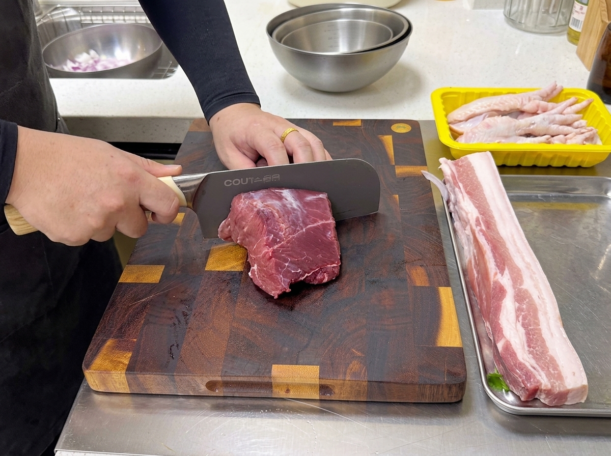 Un chef utiliza un cuchillo profesional grande para cortar un trozo de aguja de ternera cruda sobre una tabla de madera.