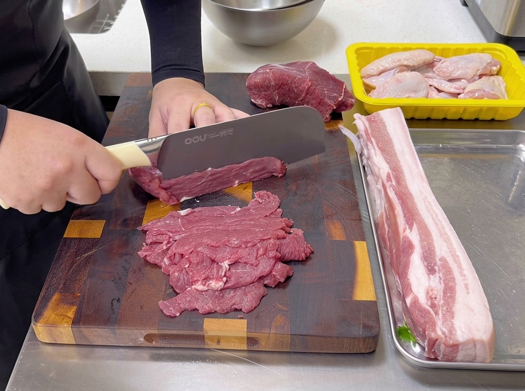 Cortando ternera cruda en láminas finas contra la fibra en una tabla de cortar de madera con un cuchillo de chef.