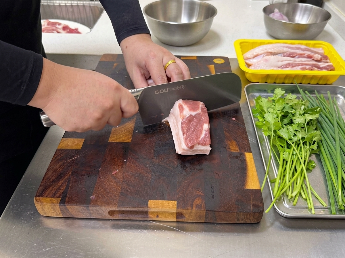 Una persona utiliza un cuchillo de cocina grande para cortar un bloque de panceta cruda veteada en tiras finas sobre una tabla de cortar.