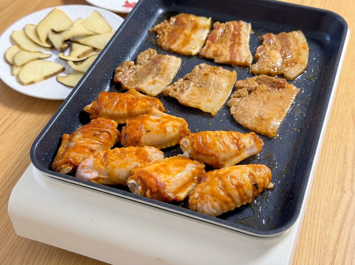 Láminas de panceta marinada y alitas de pollo Orleans de color naranja chisporrotean juntas en una parrilla eléctrica caliente.