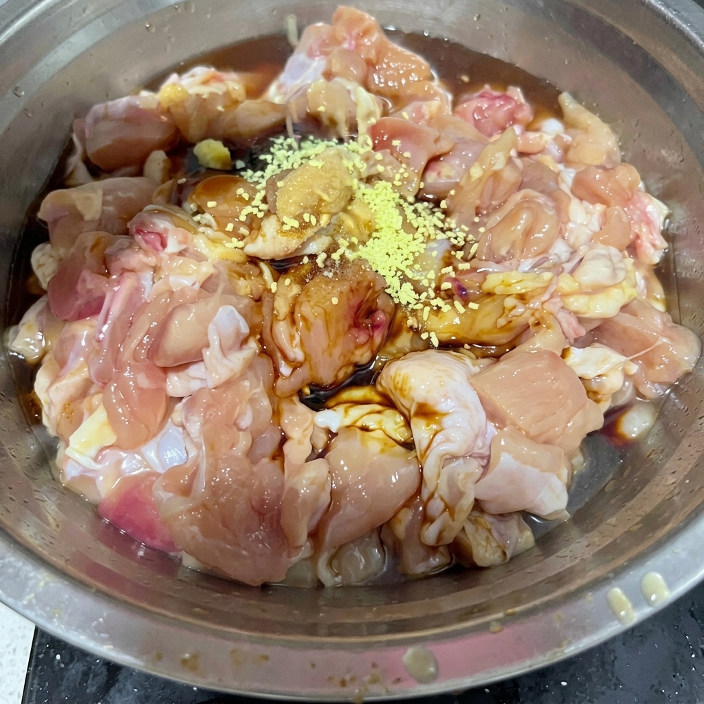 Caldo de pollo amarillo en polvo y sal blanca espolvoreados sobre los trozos de pollo crudo en un tazón de metal.