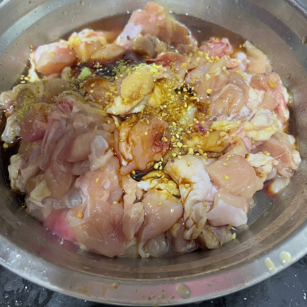 Una cucharada de mezcla seca de sazonador para barbacoa esparcida sobre trozos de pollo marinado dentro de un tazón de acero inoxidable.