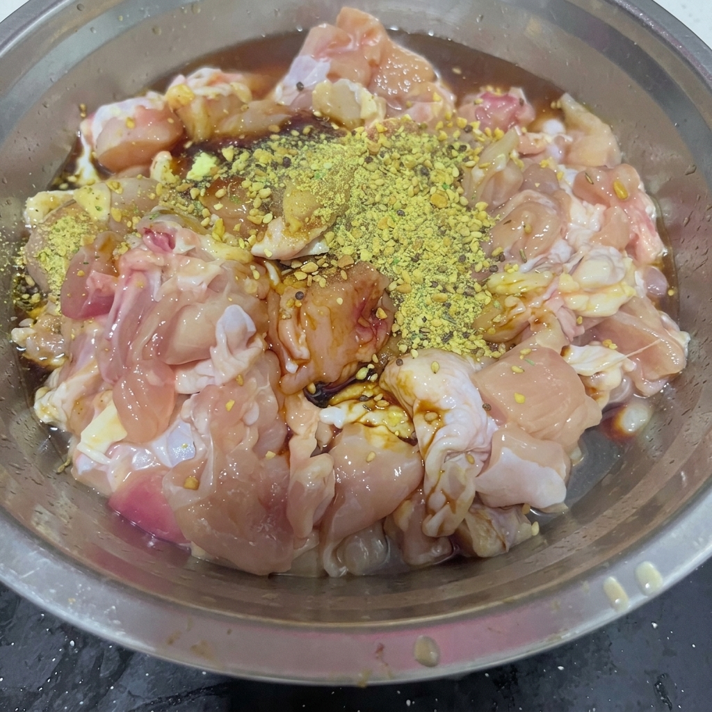 Azúcar blanco granulado espolvoreado sobre la mezcla de contramuslos de pollo sazonados en un tazón de acero inoxidable.