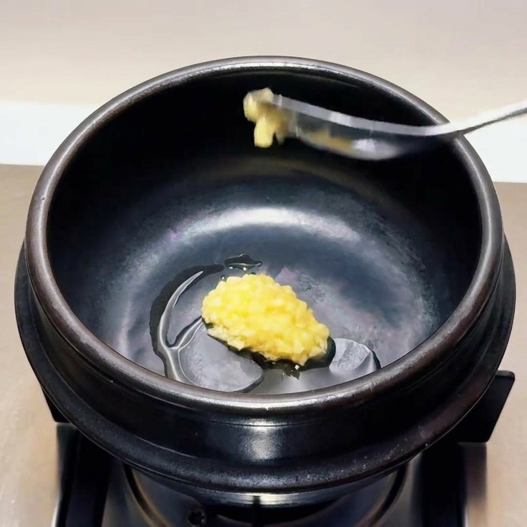 Una cucharada de ajo finamente picado colocándose en el aceite caliente dentro de una olla de piedra negra.
