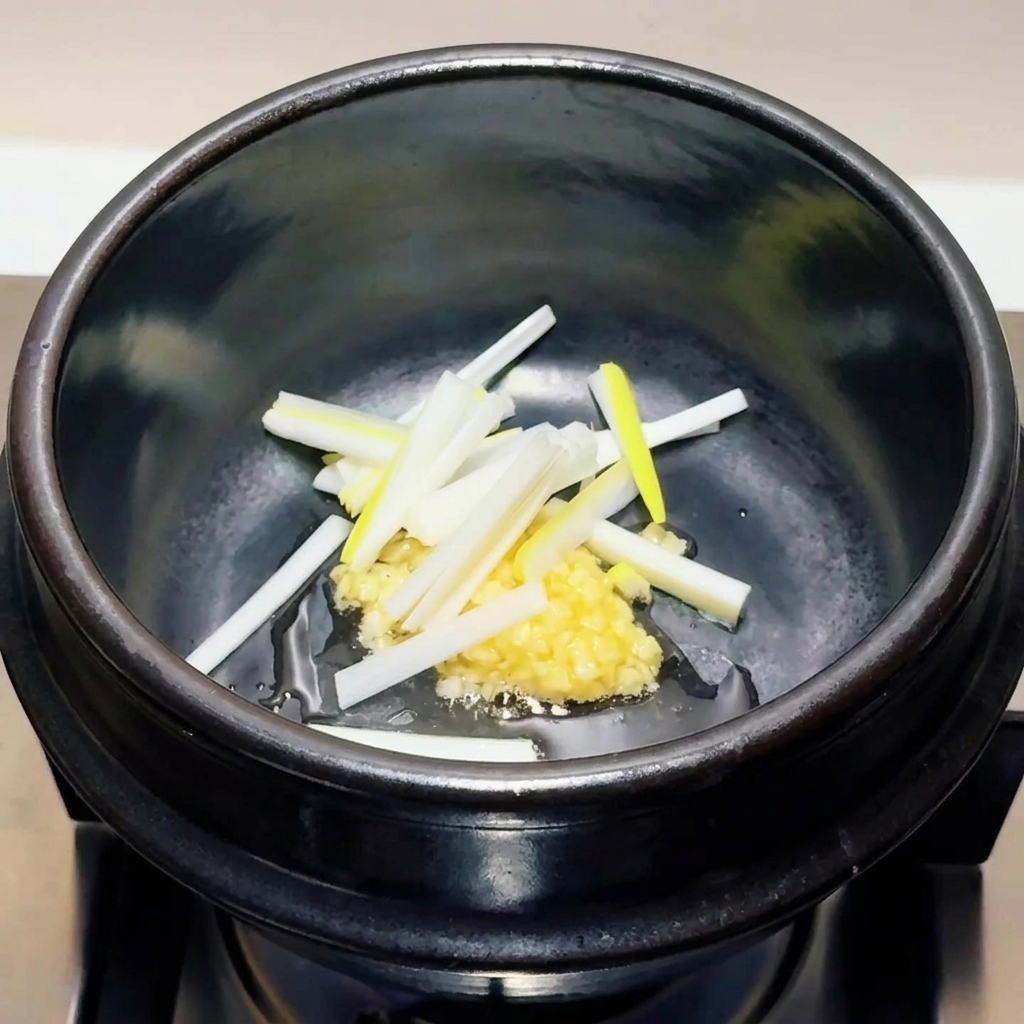 Tiras finas de brotes de ajo tierno de color verde claro y blanco sobre una porción de ajo picado en una olla negra.