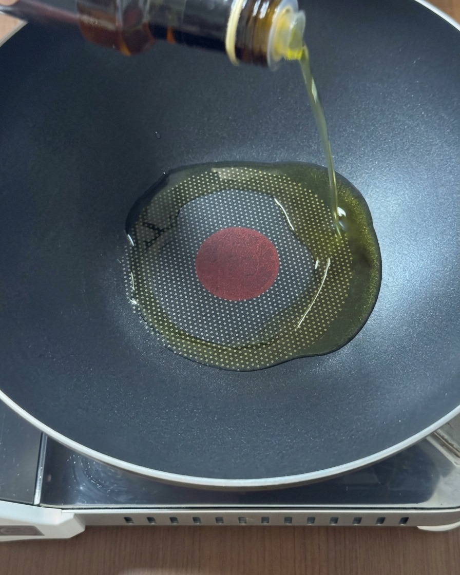 Vertiendo aceite dorado desde una botella de vidrio en el centro de un wok negro caliente.