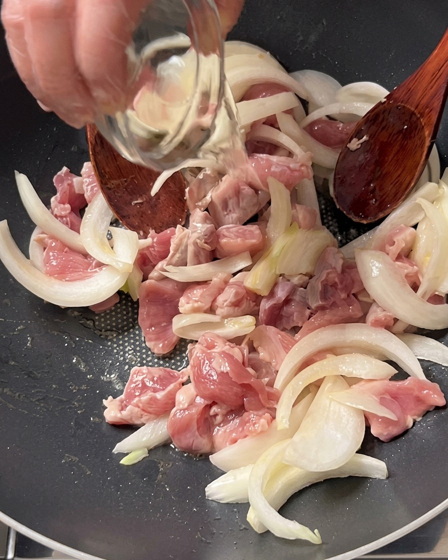 Vino de cocina siendo vertido desde un pequeño cuenco de vidrio sobre la carne de cerdo y las cebollas en la olla.