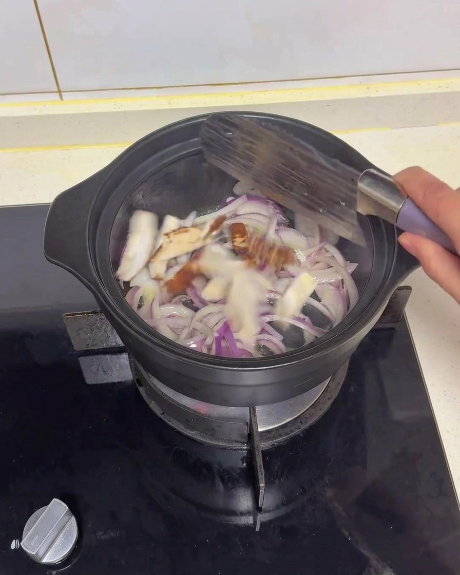 Champiñones shiitake en rodajas salteándose con cebolla morada en una cazuela negra usando una espátula.