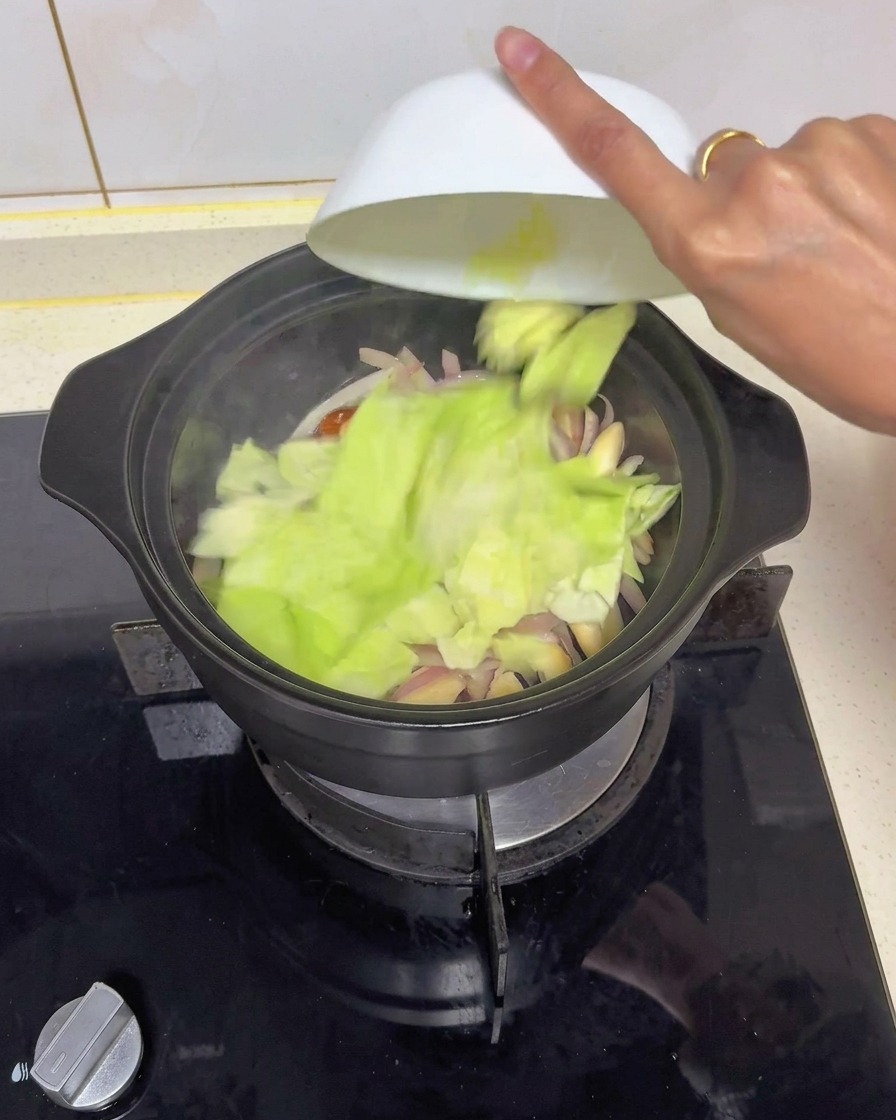 Trozos picados de repollo verde fresco volcándose desde un cuenco blanco en una cazuela negra con cebolla y champiñones salteados.