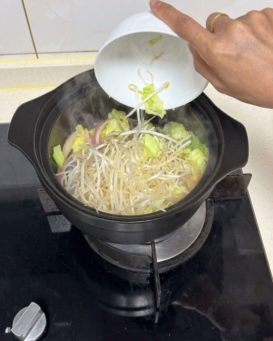 Un montón de brotes de soja frescos cayendo desde un cuenco de cerámica blanca en una cazuela negra humeante con verduras salteadas.