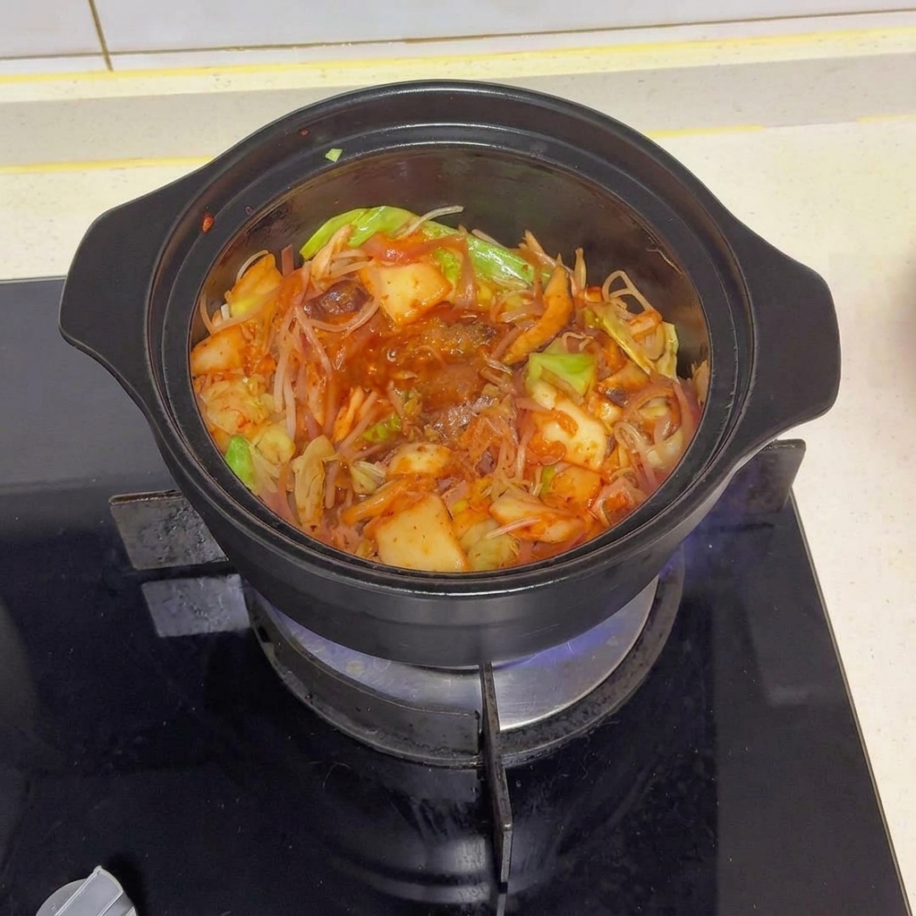 Una cazuela negra llena de verduras salteadas y kimchi, coronada con varios condimentos y chile rojo en polvo.