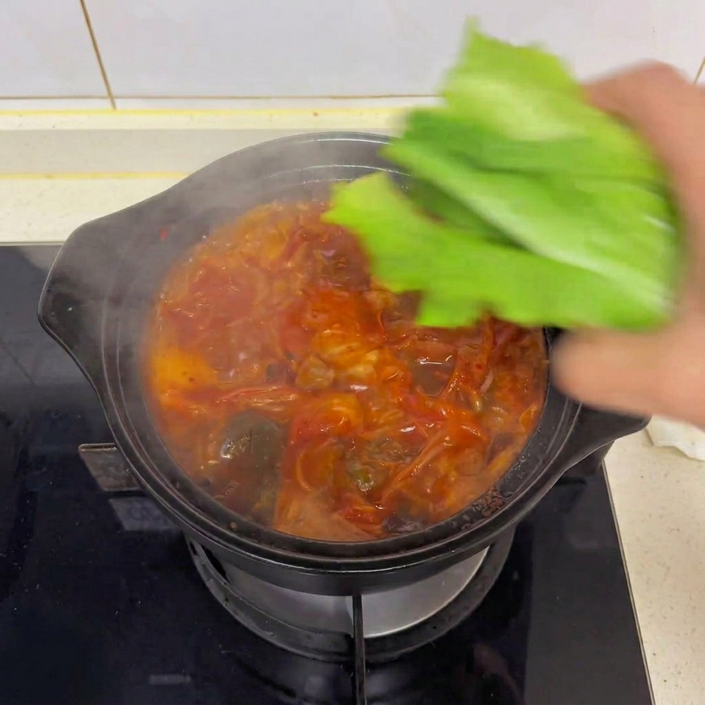 Una mano dejando caer hojas frescas de lechuga romana verde en una cazuela humeante de sopa de kimchi y tofu.