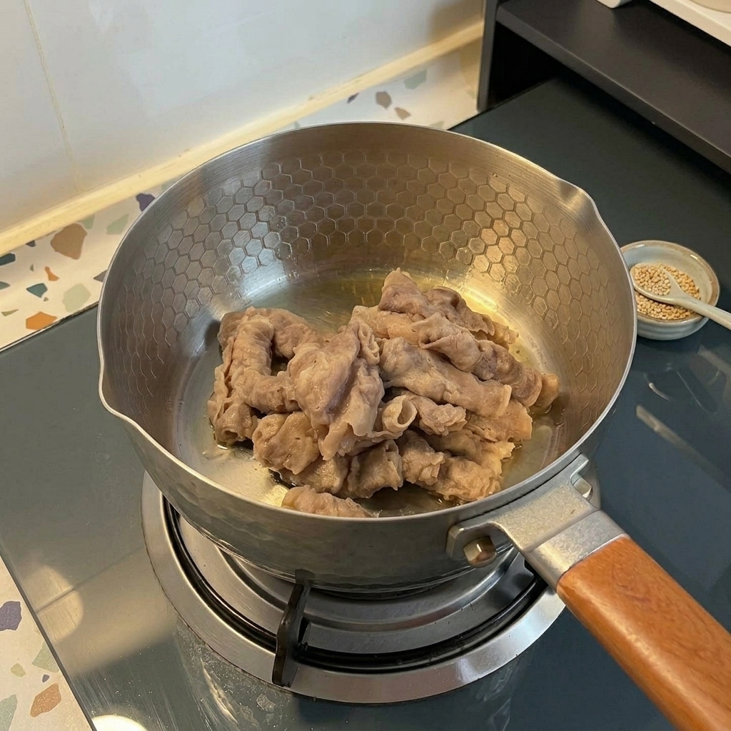 Tiras finas de carne de res salteándose en una olla de acero inoxidable sobre una estufa de gas.