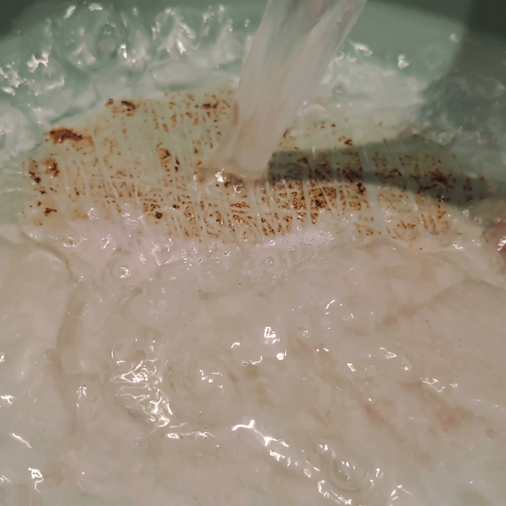 Agua de arroz turbia vertiéndose directamente en una olla de cocina, creando suaves ondas y burbujas en el líquido.